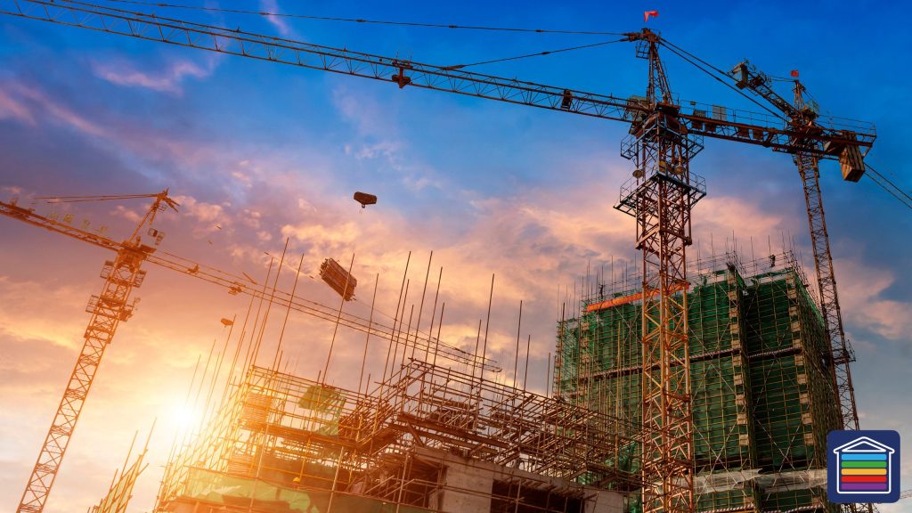 Image shows an active building site with scaffolding and multiple cranes at sunset